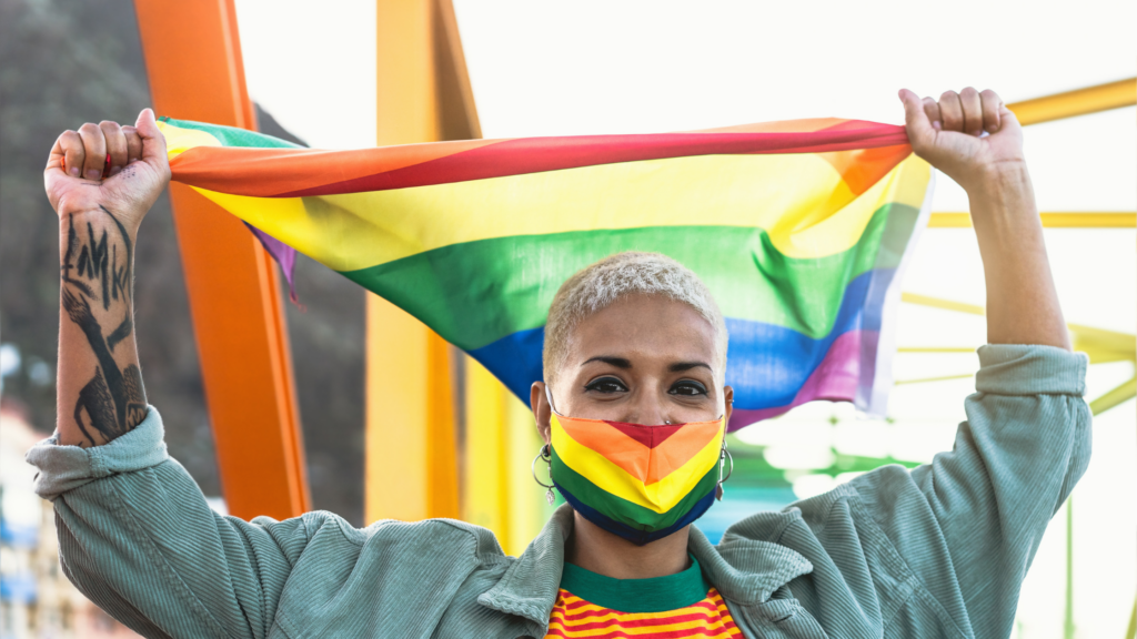 person wearing LGBTQ+ pride mask and holding pride flag